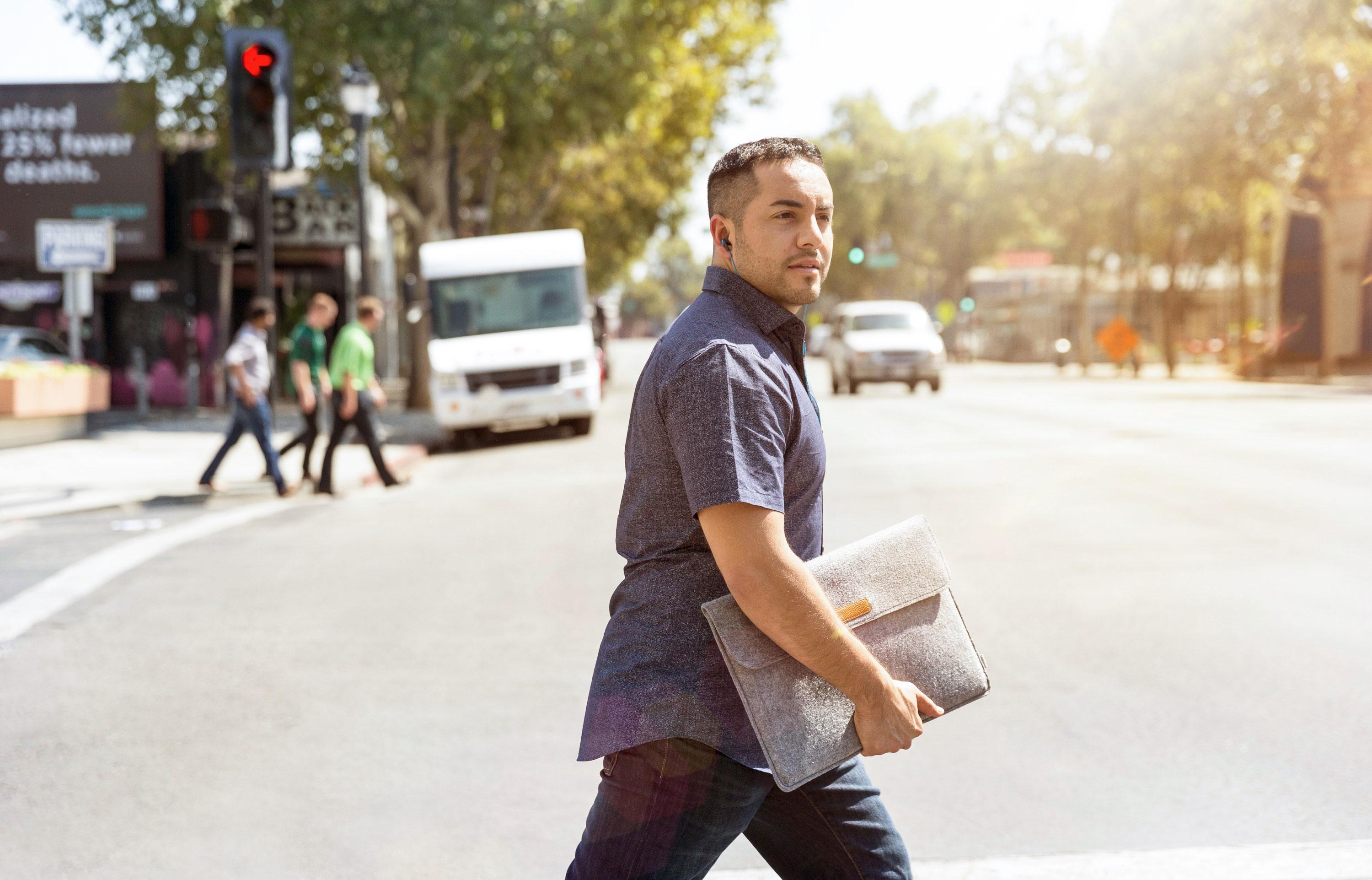 Male walking across the street holding a laptop sleeve
